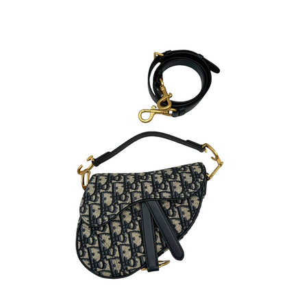 Borsa Saddle Dior in tessuto beige con trama Dior Oblique nera e blu, finiture in pelle blu notte e parti metalliche dorate. Munita di manico singolo e tracolla regolabile, e amovibile. Completa di corredo. Originale, usato, condizioni ottime. 