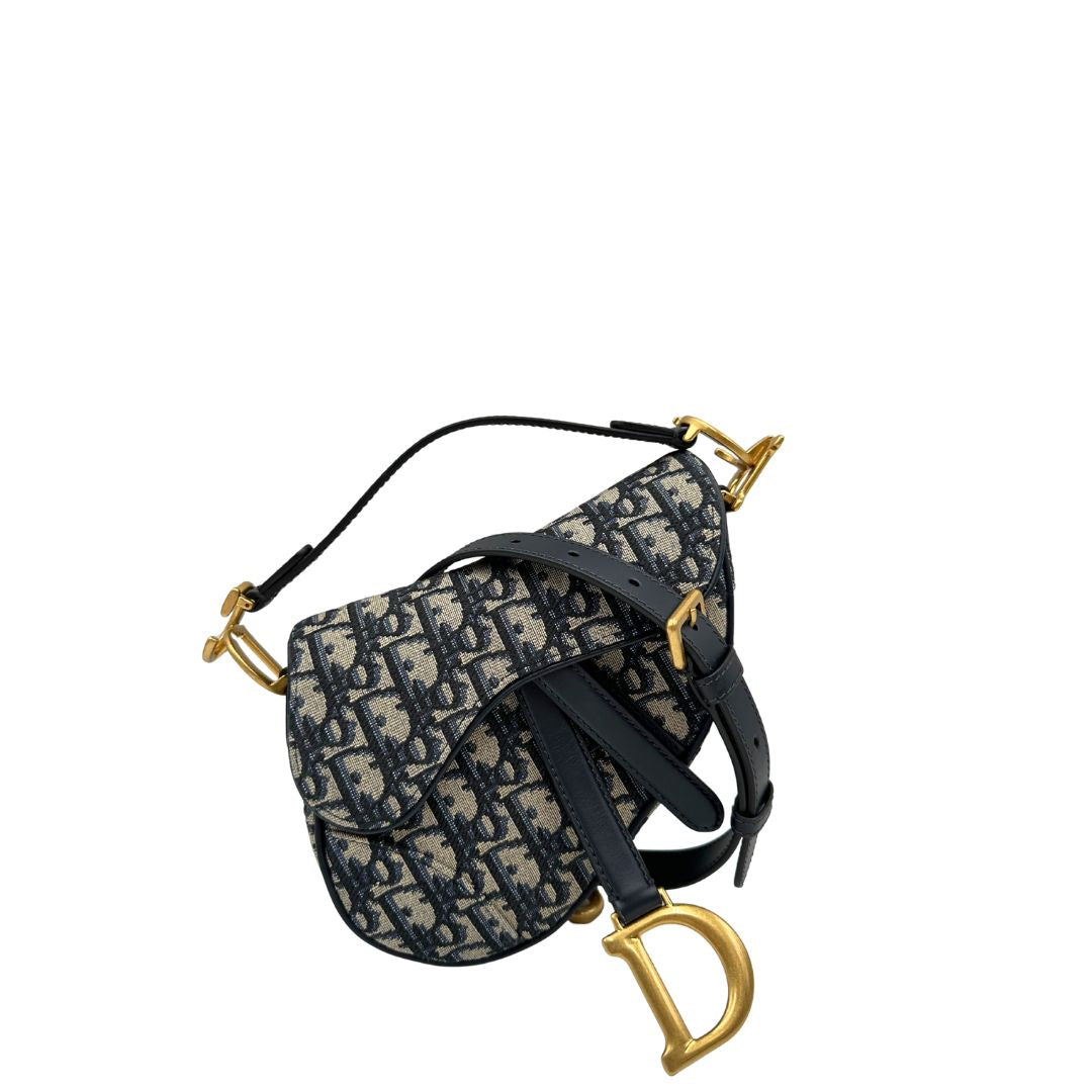 Borsa Saddle Dior in tessuto beige con trama Dior Oblique nera e blu, finiture in pelle blu notte e parti metalliche dorate. Munita di manico singolo e tracolla regolabile, e amovibile. Completa di corredo. Originale, usato, condizioni ottime. 