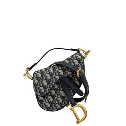Borsa Saddle Dior in tessuto beige con trama Dior Oblique nera e blu, finiture in pelle blu notte e parti metalliche dorate. Munita di manico singolo e tracolla regolabile, e amovibile. Completa di corredo. Originale, usato, condizioni ottime. 