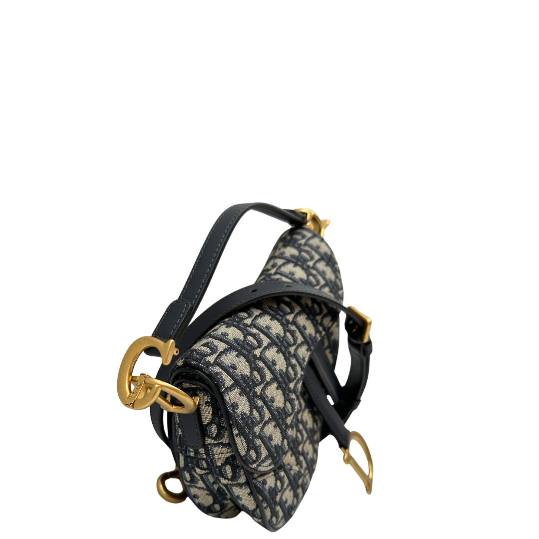 Borsa Saddle Dior in tessuto beige con trama Dior Oblique nera e blu, finiture in pelle blu notte e parti metalliche dorate. Munita di manico singolo e tracolla regolabile, e amovibile. Completa di corredo. Originale, usato, condizioni ottime. 
