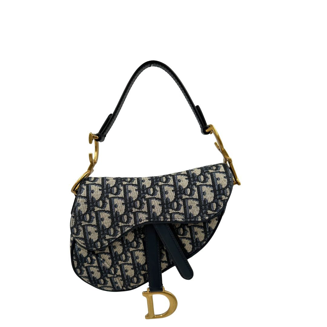 Borsa Saddle Dior in tessuto beige con trama Dior Oblique nera e blu, finiture in pelle blu notte e parti metalliche dorate. Munita di manico singolo e tracolla regolabile, e amovibile. Completa di corredo. Originale, usato, condizioni ottime. 