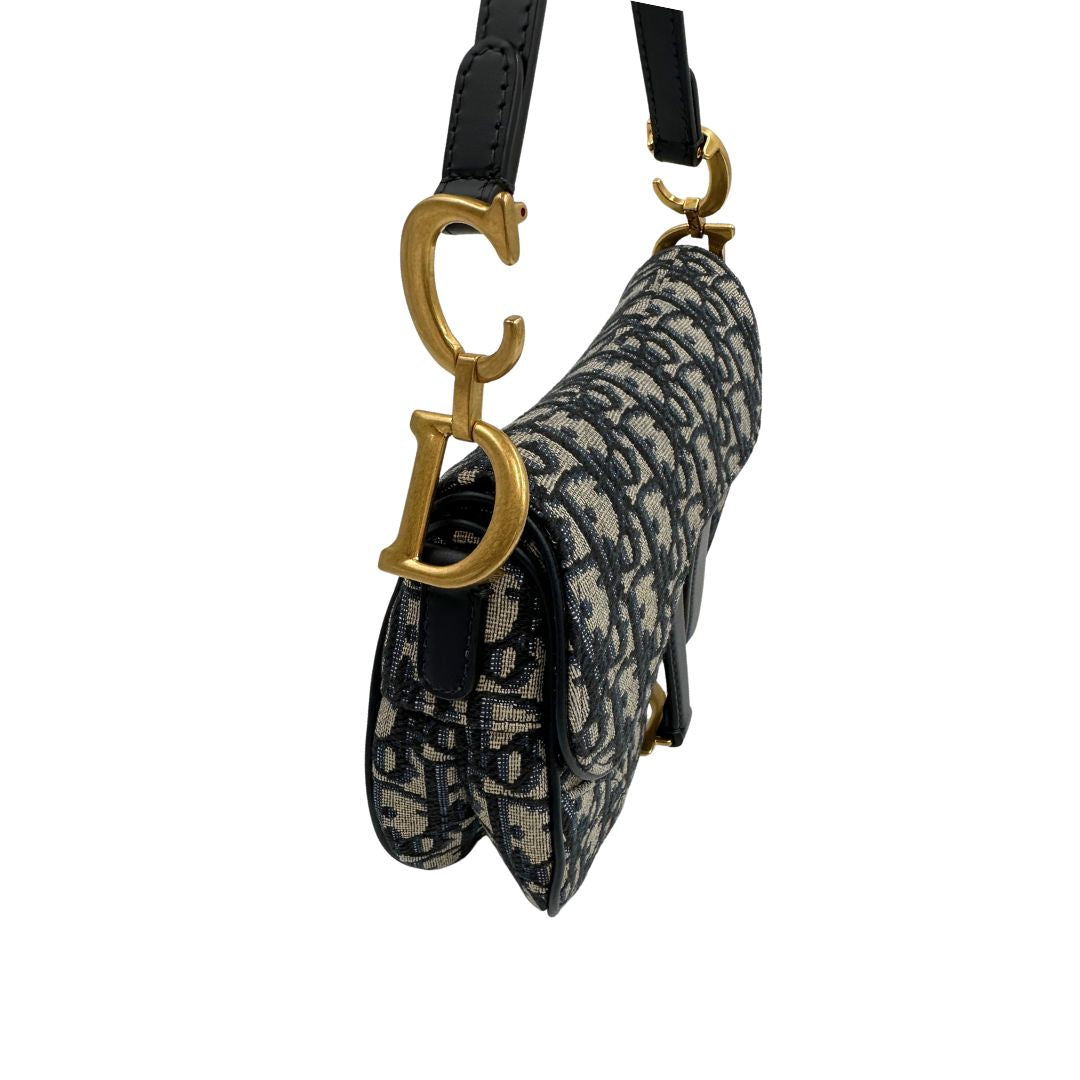 Borsa Saddle Dior in tessuto beige con trama Dior Oblique nera e blu, finiture in pelle blu notte e parti metalliche dorate. Munita di manico singolo e tracolla regolabile, e amovibile. Completa di corredo. Originale, usato, condizioni ottime. 