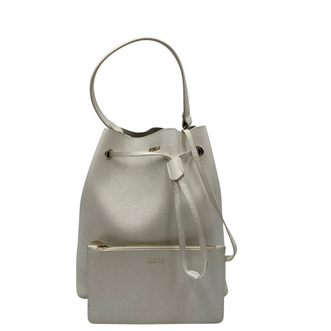Front di un bucket Furla in pelle bianco gesso con parti metalliche dorate; munito di un manico singolo e pochette estraibile ed amovibile. Completo di dustbag.
