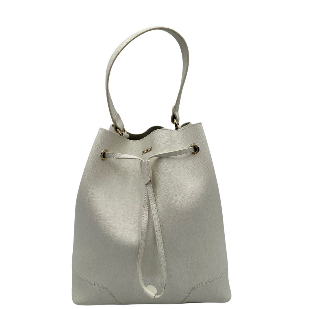 Front di un bucket Furla in pelle bianco gesso con parti metalliche dorate; munito di un manico singolo e pochette estraibile ed amovibile. Completo di dustbag.