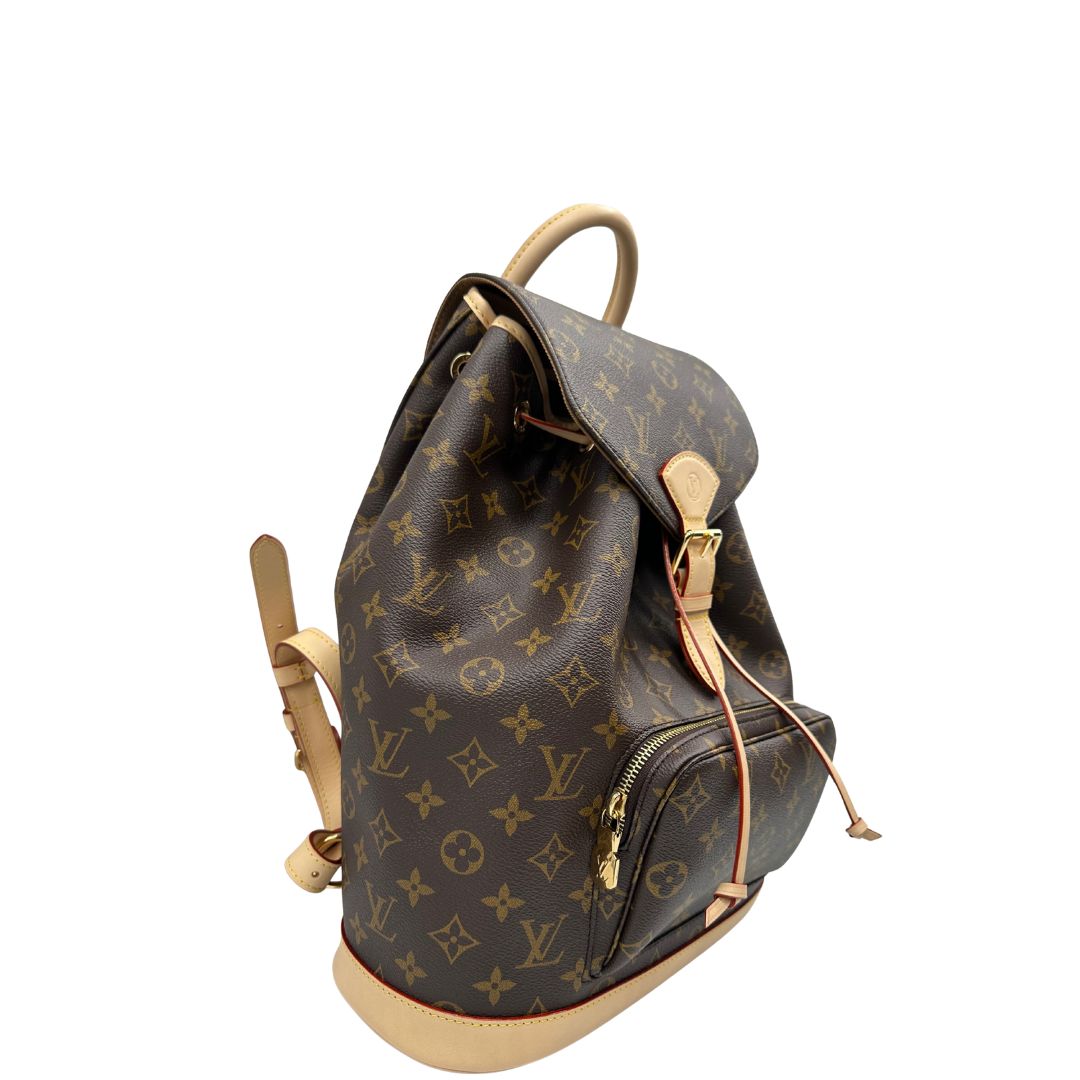 Laterale sinistro di uno zaino LV in canvas marrone monogram con finiture in vacchetta naturale e parti metalliche dorate; munito di due bretelle regolabili. Full set.