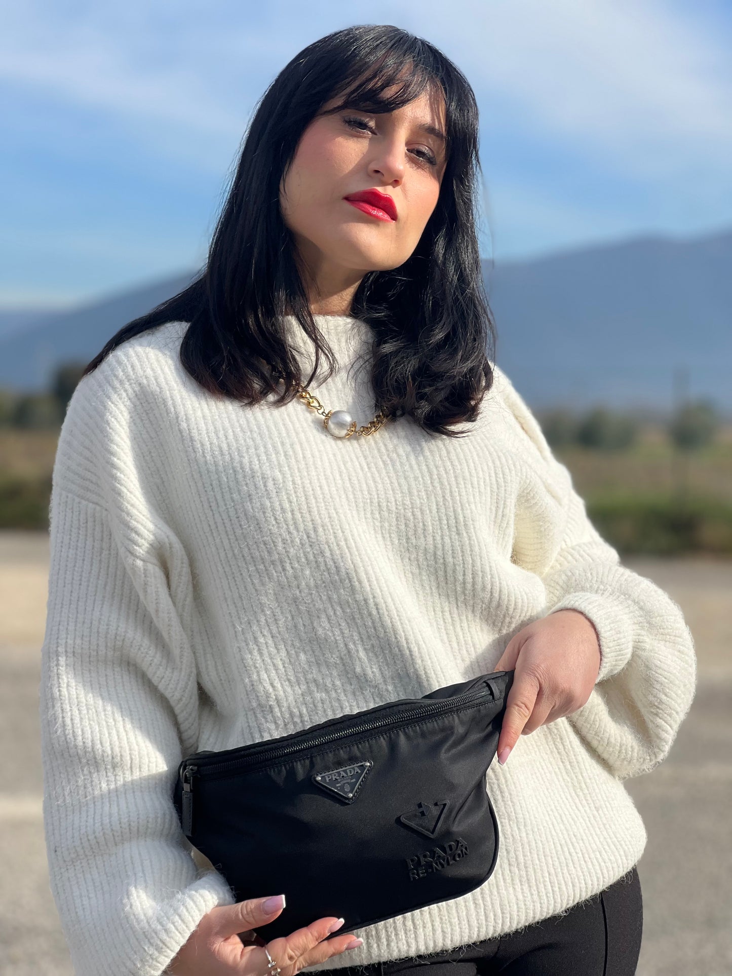 Ragazza che indossa un marsupio Prada in Re-Nylon nero con dettagli in pelle tono su tono, logo gommato sul front e parti in metallo argentato. Leggermente regolabile, indossabile a marsupio o cross body.