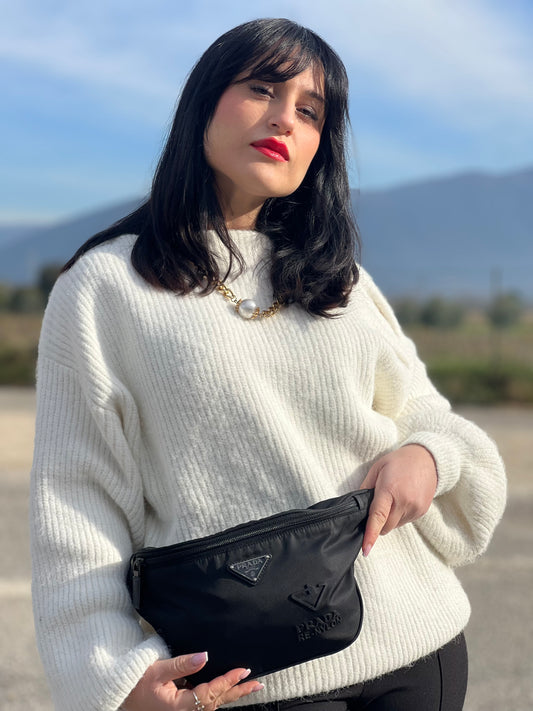 Ragazza che indossa un marsupio Prada in Re-Nylon nero con dettagli in pelle tono su tono, logo gommato sul front e parti in metallo argentato. Leggermente regolabile, indossabile a marsupio o cross body.