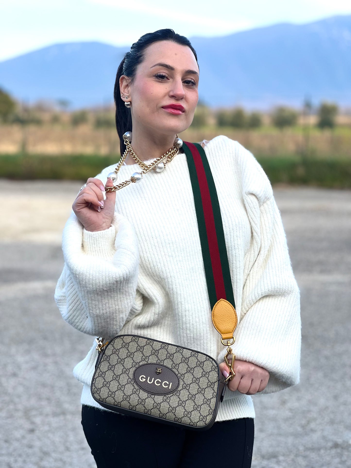 Ragazza che indossa una borsa Gucci Neo Vintage in canvas beige GG Supreme con finiture in pelle marrone e parti metalliche dorate. Munita di una tracolla in tessuto Web verde e rosso, con dettagli in pelle gialla. Rifinita con logo lettering sul front e testa di tigre decorativa. Completa di dustbag.