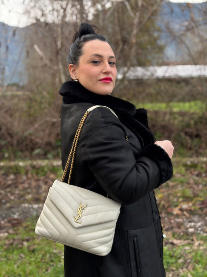 Ragazza che indossa una borsa Saint Laurent in pelle trapuntata bianco latte con tracolla scorrevole in catena e spallacci in pelle, con parti metalliche dorate e iconico logo Cassandre sul front. Completa di dustbag. Indossabile a spalla o a tracolla.