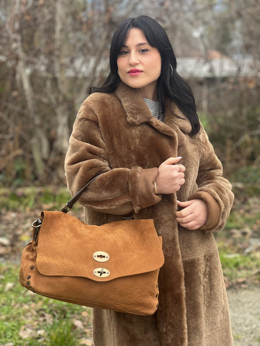 Ragazza che indossa una borsa Postina M Zanellato in pelle scamosciata color cannella con finiture marroni testa di moro e parti metalliche bronzo; munita di un manico singolo . Completa di dustbag.