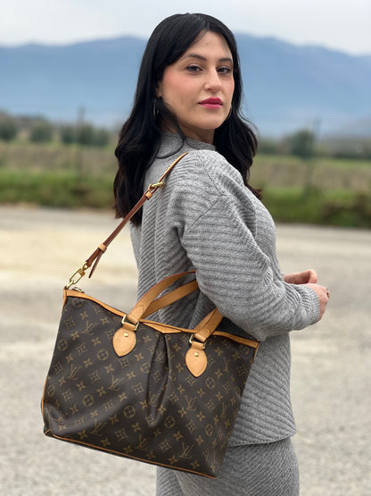 Ragazza che indossa una borsa Louis Vuitton in canvas marrone monogram con parti metalliche dorate e finiture in vacchetta naturale; munita di una tracolla amovibile e regolabile e doppi manici. Indossabile a spalla oppure a mano.