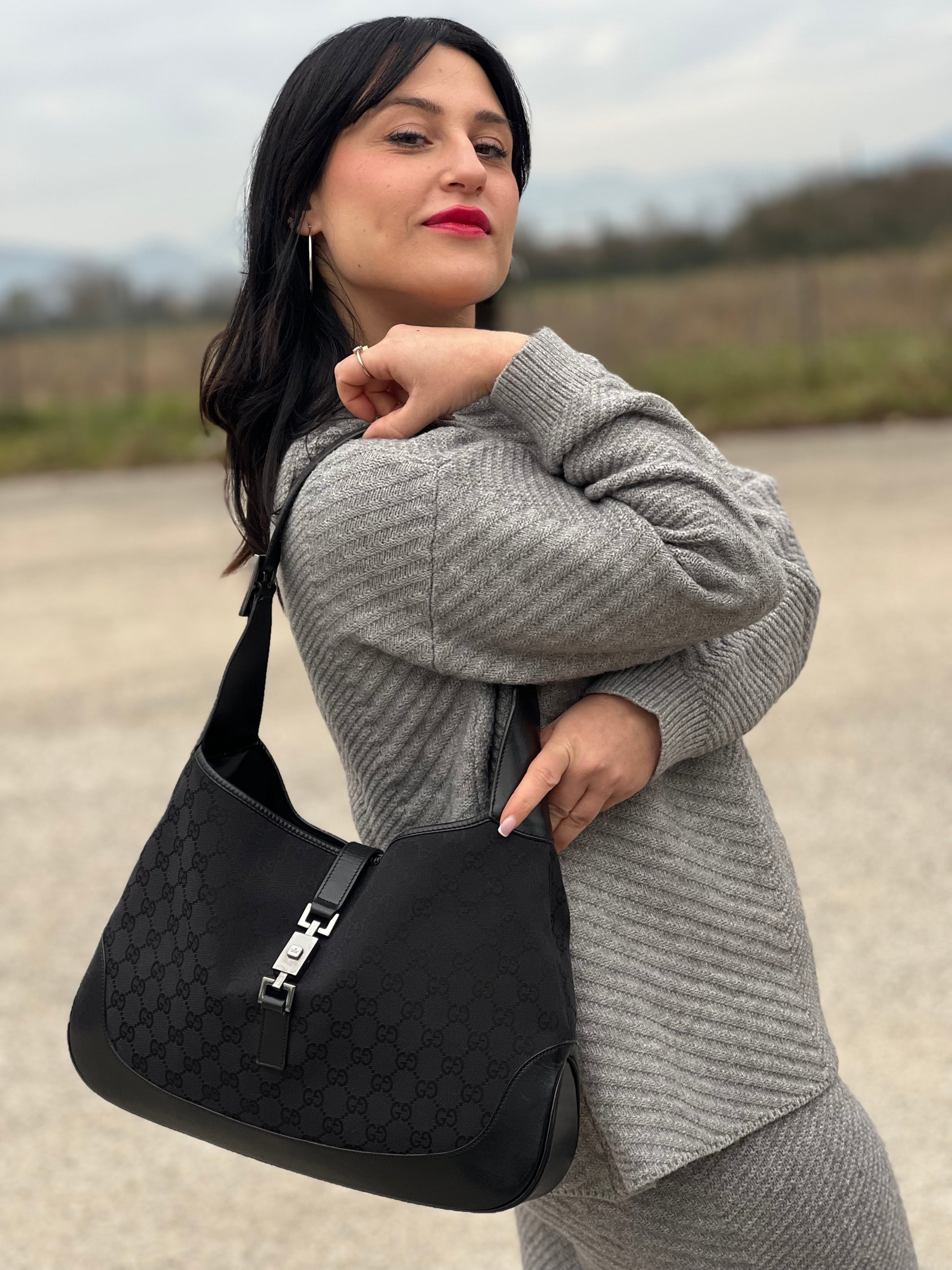 Ragazza che indossa una borsa Gucci in tessuto nero GG con finiture in pelle tono su tono e parti metalliche argentate. Munita di un manico leggermente regolabile.