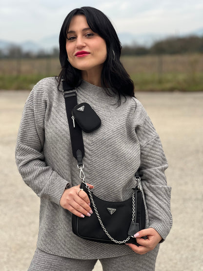 Ragazza che indossa una borsa Prada in nylon nero con parti metalliche argentate e finiture in pelle tono su tono; munita di una mini pouch amovibile, un accessorio portachiavi, manico in catena e una tracolla in tessuto amovibile e regolabile.