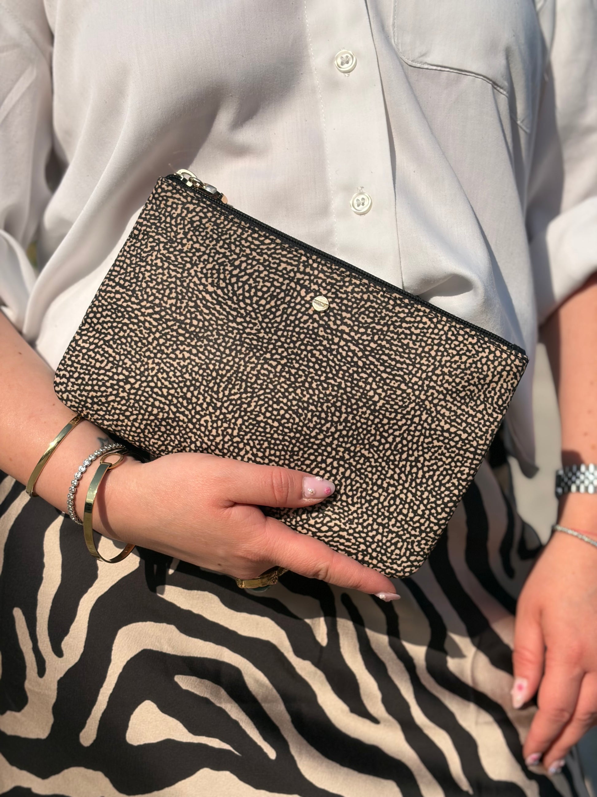 Ragazza che indossa una pochette Borbonese in tessuto nylon color beige e marrone trama occhio di pernice, usata, originale, second hand, in ottime condizioni.