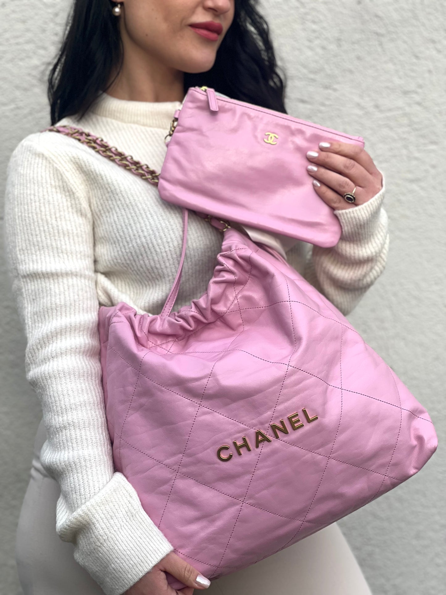 Ragazza che indossa una borsa Chanel 22 in pelle trapuntata rosa con parti metalliche dorate; dotata di pochette estraibile e amovibile, doppi manici in catena e pelle per portarla a spalla. Chiusura con bottone automatici. Completa di scatola e dustbag.