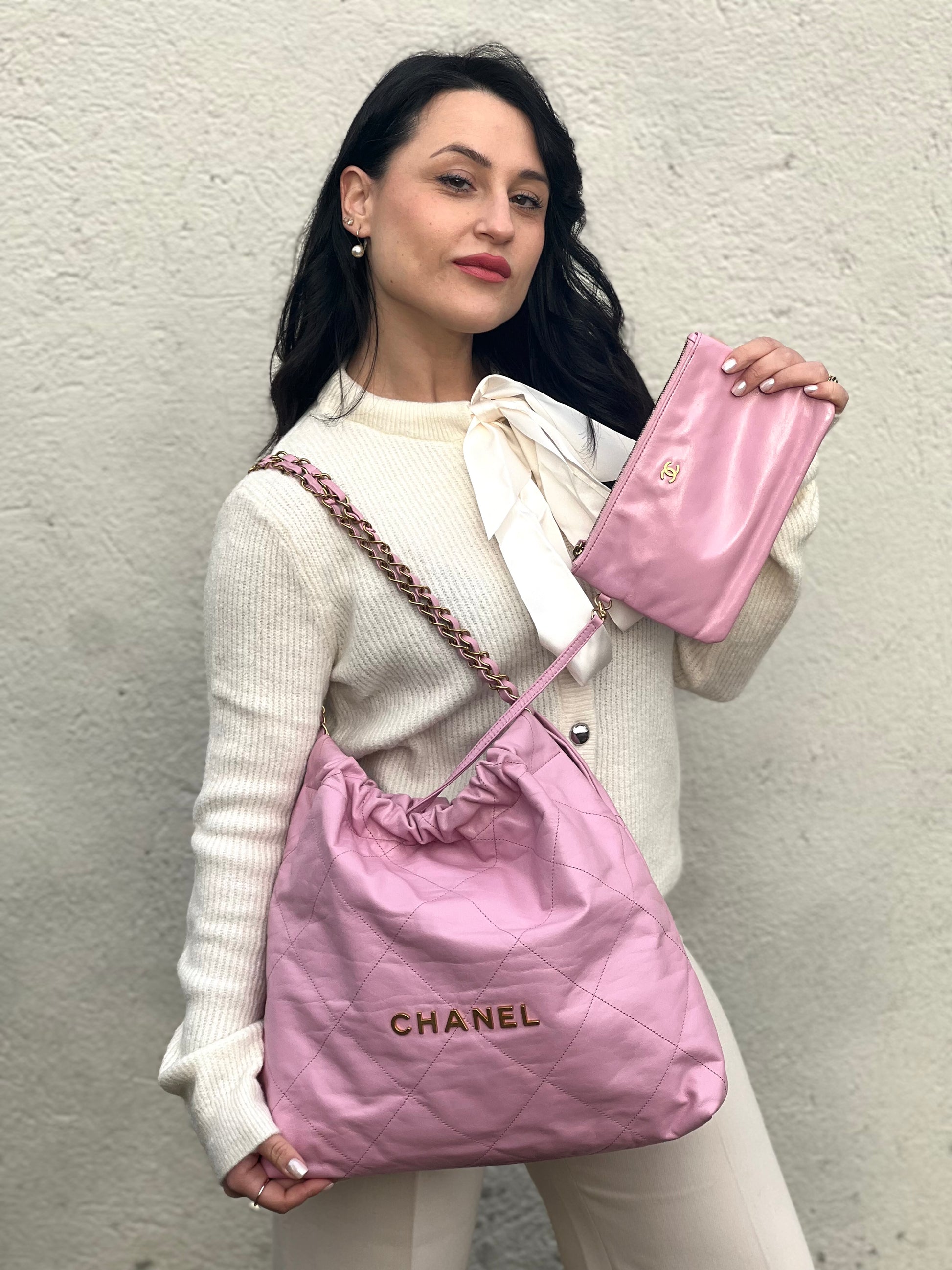 Ragazza che indossa una borsa Chanel 22 in pelle trapuntata rosa con parti metalliche dorate; dotata di pochette estraibile e amovibile, doppi manici in catena e pelle per portarla a spalla. Chiusura con bottone automatici. Completa di scatola e dustbag.