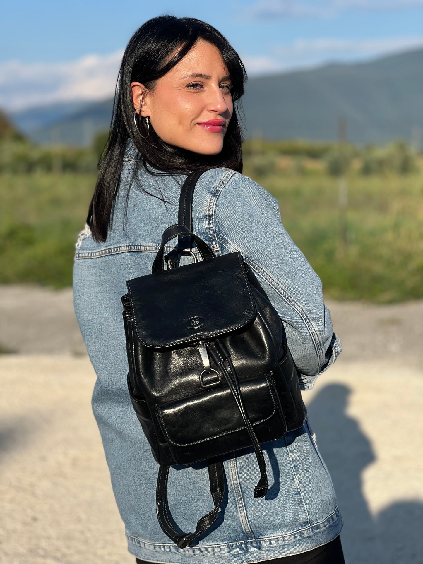 Ragazza che indossa uno zaino The Bridge in cuoio nero con parti metalliche argentate. Cinghie delle bretelle regolabili. Completo di dustbag.
