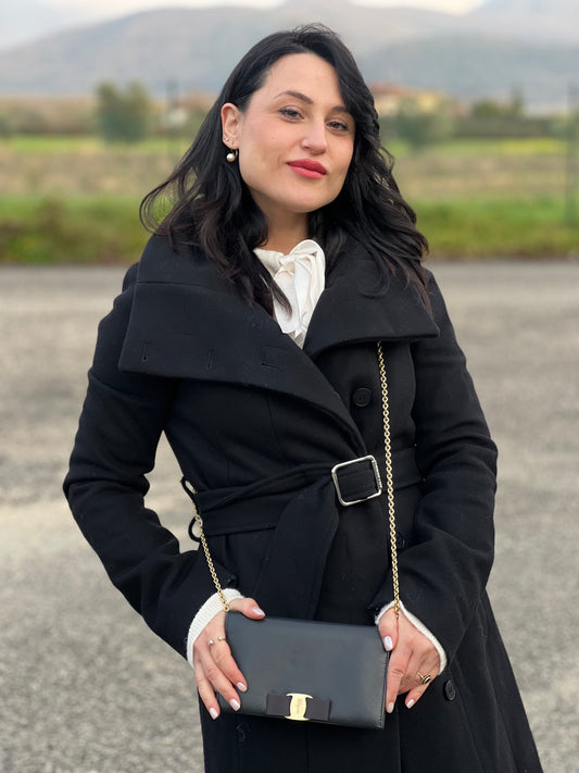 Ragazza che indossa un WOC Salvatore Ferragamo in pelle saffiano nera con parti metalliche oro. Munita di una tracolla in catena amovibile e non regolabile. Chiusura con fiocco. Completo di dustbag. Indossabile a tracolla.