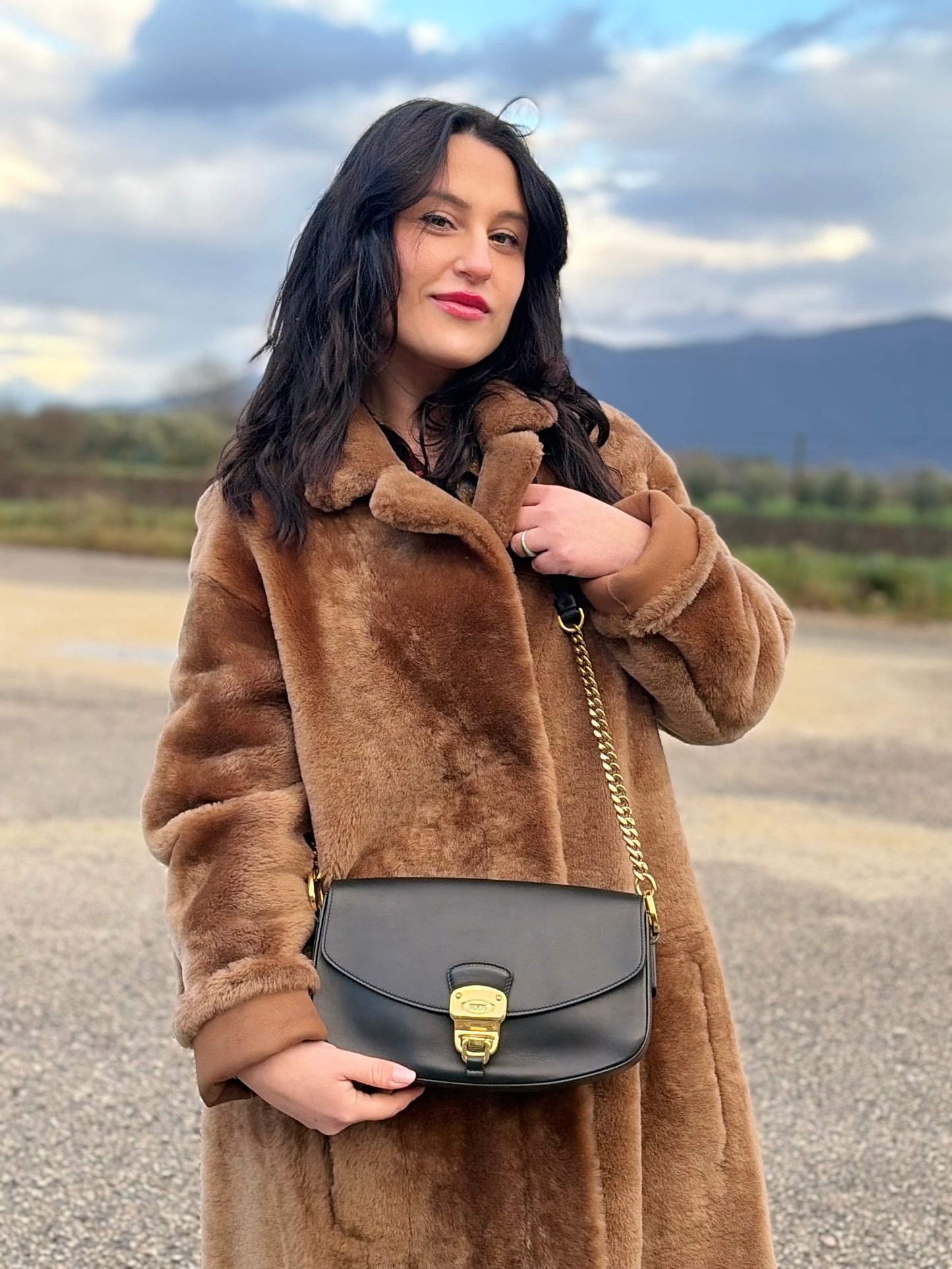 Ragazza che indossa Borsa Tod's in pelle nera con parti metalliche dorate; munita di una tracolla in catena e in pelle non amovibile e regolabile. Completa di dustbag. Originale, usata, di lusso, in ottime condizioni.