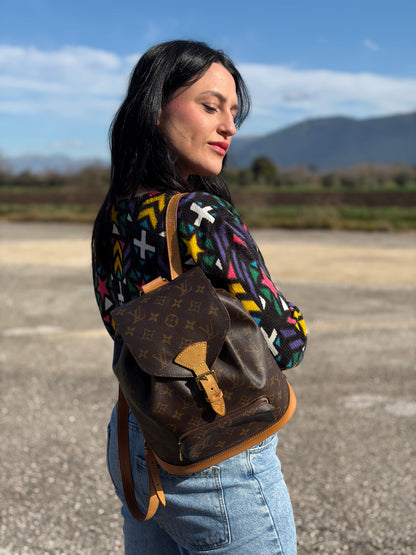 Ragazza che indossa uno zaino Montsouris mini in canvas marrone monogram con finiture in vacchetta naturale e parti metalliche dorate, munito di un anello sulla parte superiore e due bretelle in vacchetta regolabili con fibbie. Completo di dustbag.