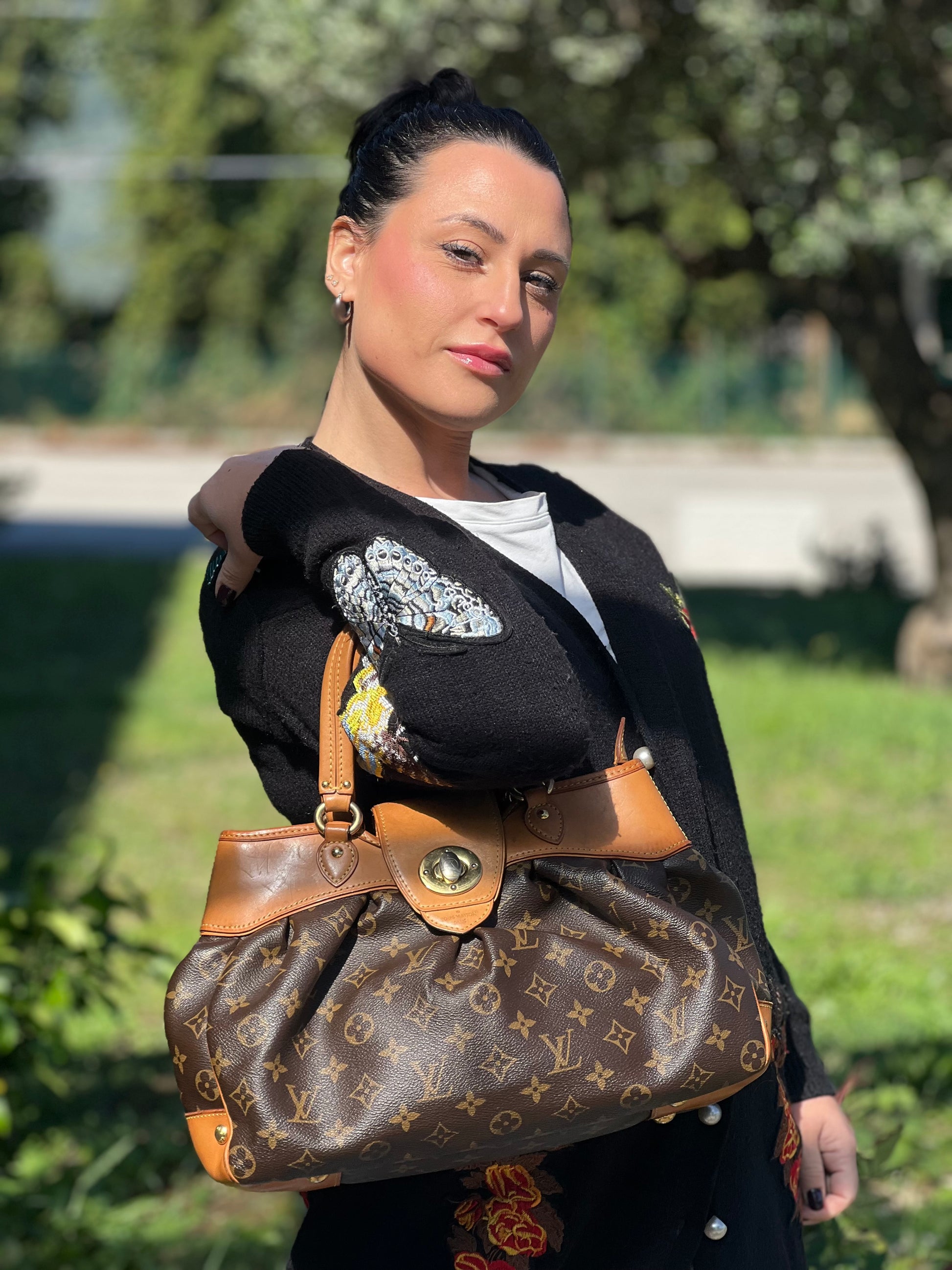 Ragazza che indossa una borsa Louis Vuitton in canvas marrone monogram con finiture in vacchetta naturale e parti metalliche dorate; munita di doppi manici stondati, da indossare a mano.