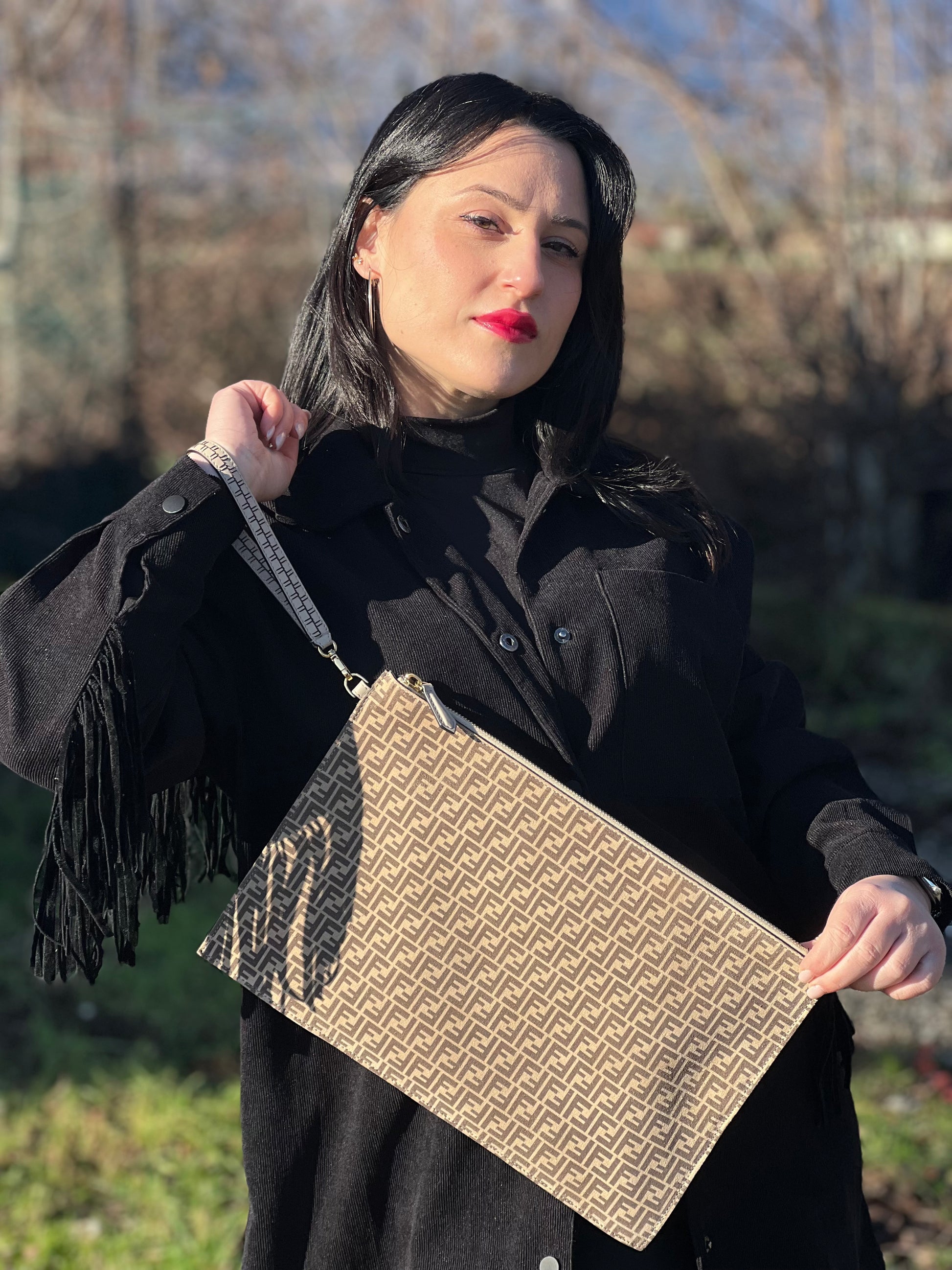 Ragazza che indossa una pochette Fendi in suede beige con trama zucchino, finiture in pelle tono su tono e parti metalliche dorate; munita di un polsino amovibile, da portare a mano. Completa di dustbag.