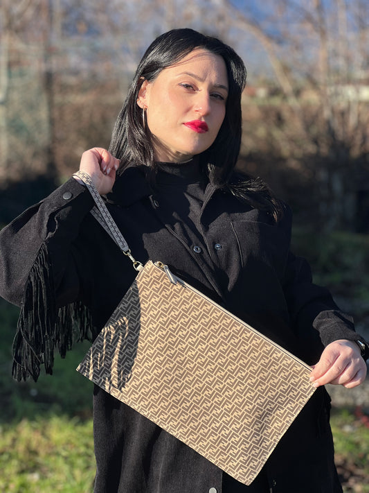 Ragazza che indossa una pochette Fendi in suede beige con trama zucchino, finiture in pelle tono su tono e parti metalliche dorate; munita di un polsino amovibile, da portare a mano. Completa di dustbag.
