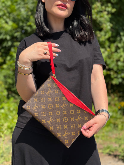 Ragazza che indossa una pochette Louis Vuitton con scomparti interni portacarte, in canvas marrone monogram e dettagli rossi, con parti metalliche dorate, usata, originale, second hand, in ottime condizioni.