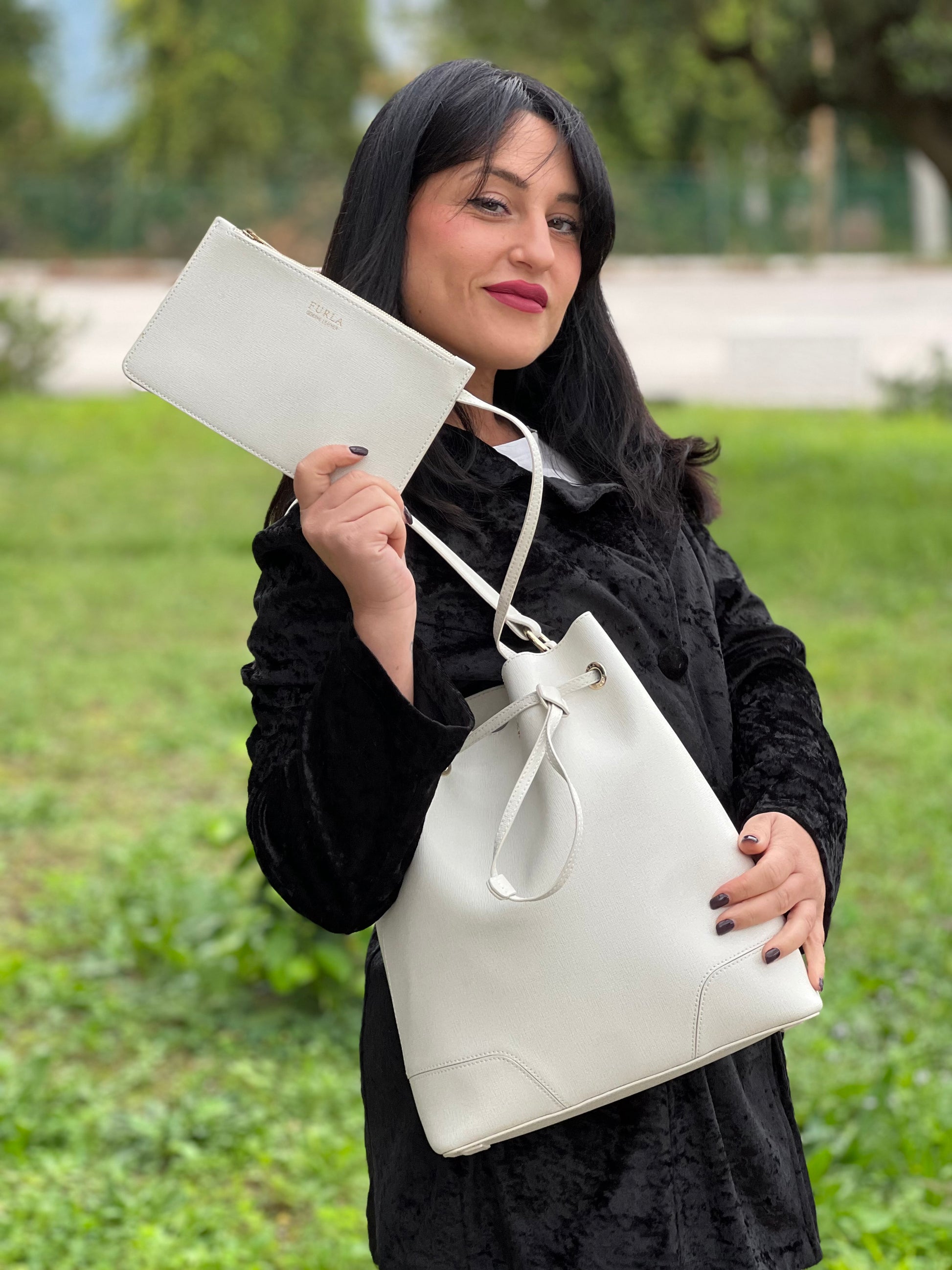 Ragazza che indossa un bucket Furla in pelle bianco gesso con parti metalliche dorate; munito di un manico singolo e pochette estraibile ed amovibile. Completo di dustbag.