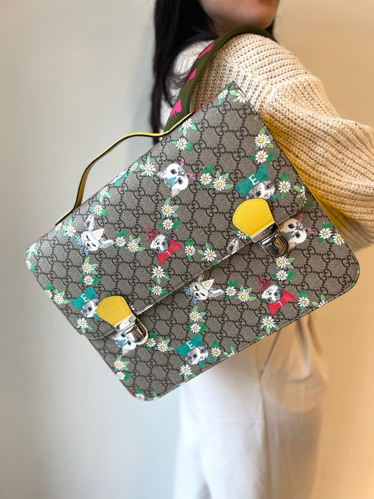 Ragazza che indossa uno zaino Gucci Kids in canvas monogram GG beige con stampa floreale e animaletti; finiture e interno in pelle gialla. Chiusura a patta con doppi ganci e parti metalliche argentate; dotato di manico superiore e doppie bretelle regolabili in tessuto verde oliva con ricami a farfalle fucsia. Completo di scatola e dustbag.