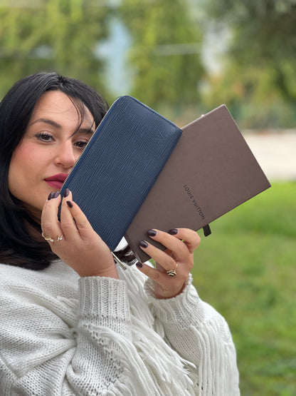 Ragazza che mostra un portafoglio Louis Vuitton in pelle Epi blu marino con parti metalliche argentate. Completo di corredo.