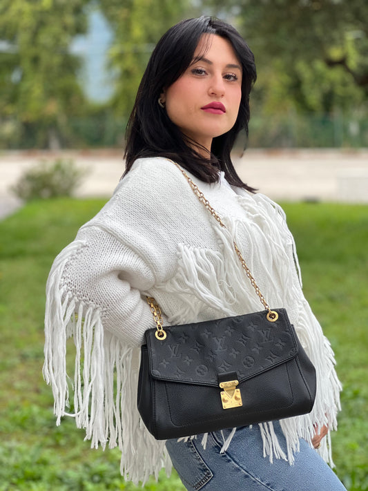 Ragazza che indossa una borsa Louis Vuitton in pelle nera monogram Empreinte con parti metalliche dorate; munita di una tracolla scorrevole in catena. Indossabile a spalla e a tracolla.