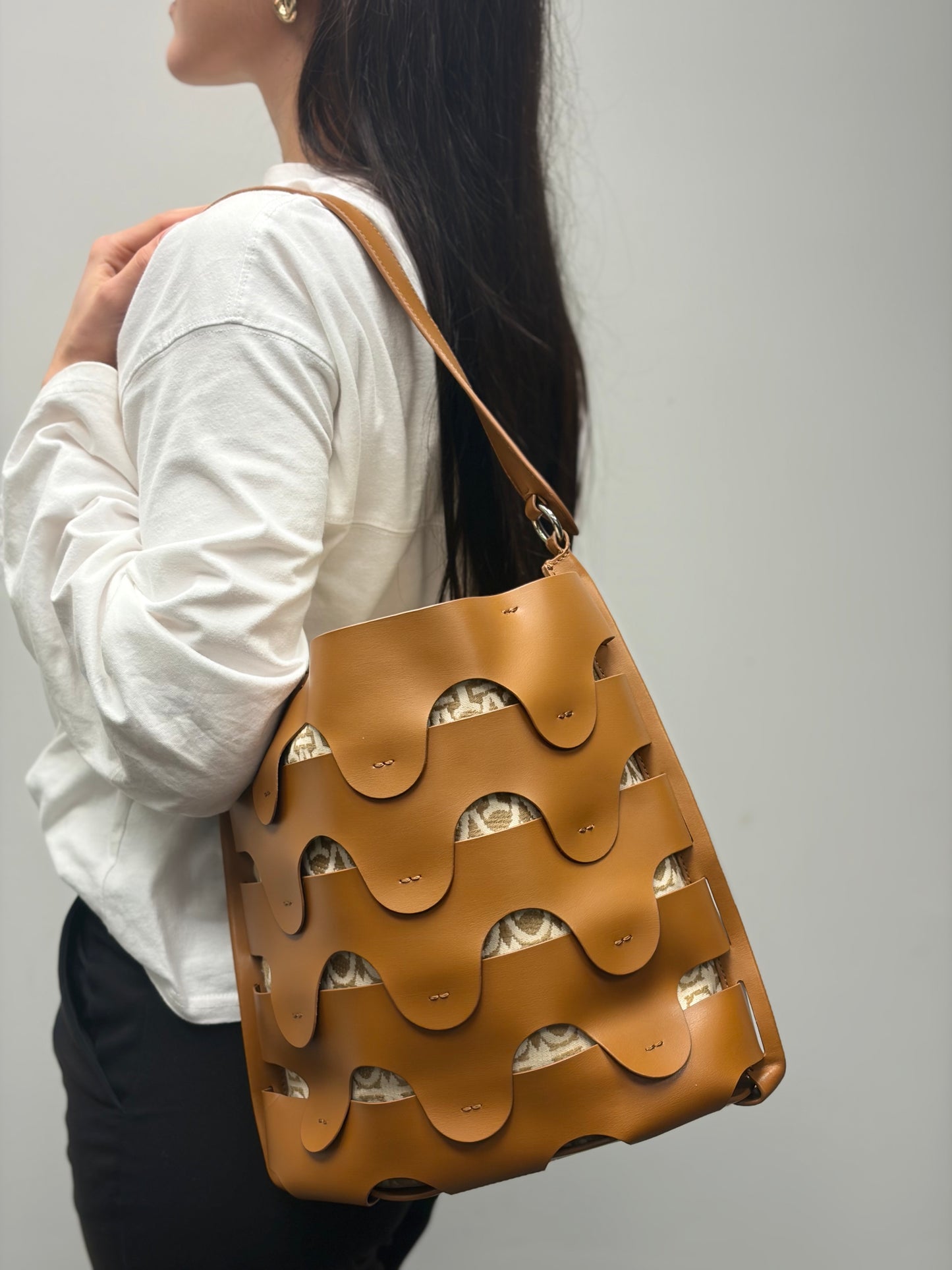 Razza che indossa una borsa Coccinelle in pelle color cammello con parti metalliche argentate e interno in tessuto logato; munita di un manico singolo leggermente regolabile. Indossabile a spalla.