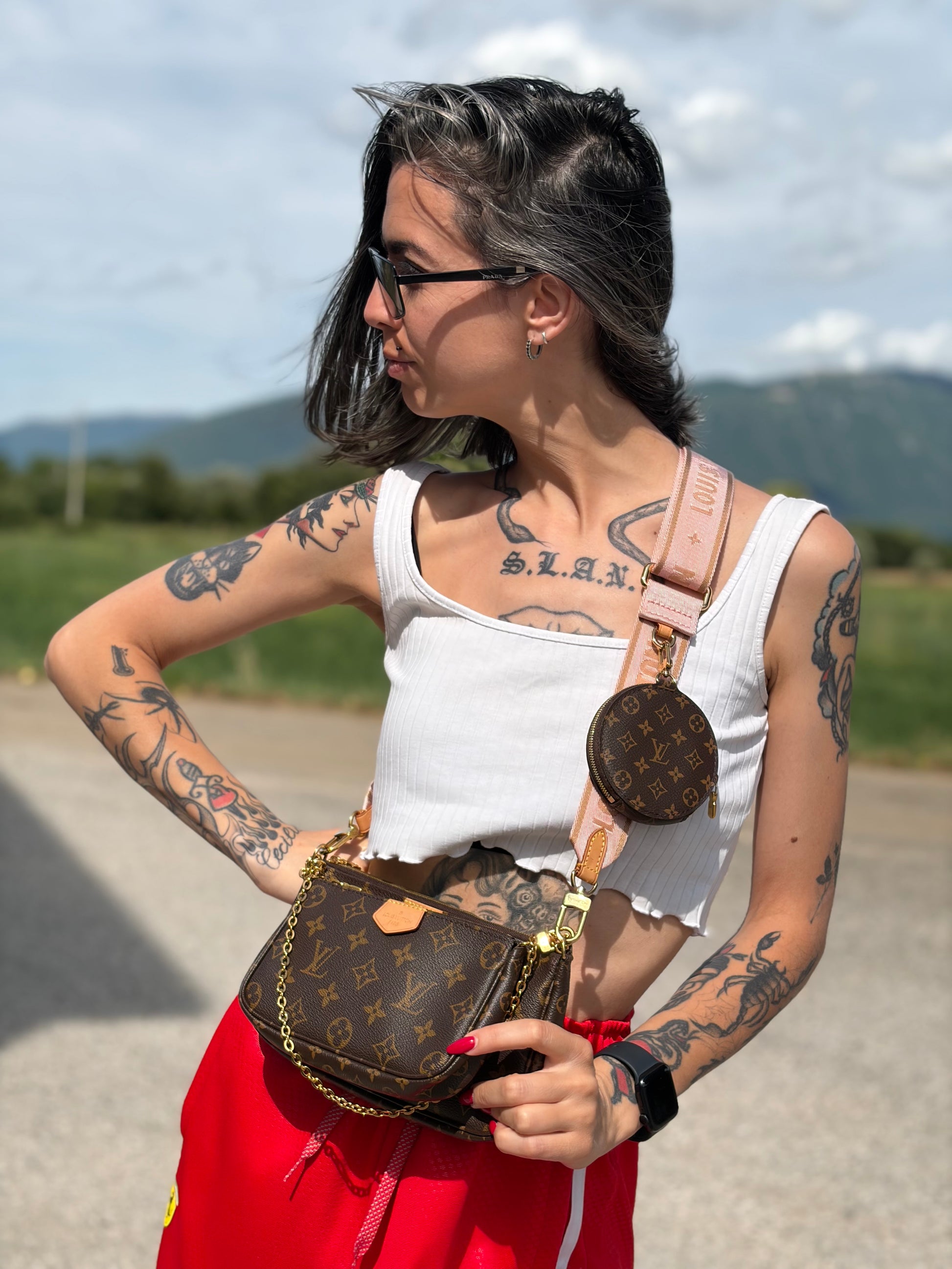 Ragazza che indossa una Multi Pochette Accessoires Louis Vuitton in canvas marrone monogram con dettagli in vacchetta naturale, manico in catena dorata e tracolla in tessuto Jacquard rosa, usata, originale, second hand, in ottime condizioni.