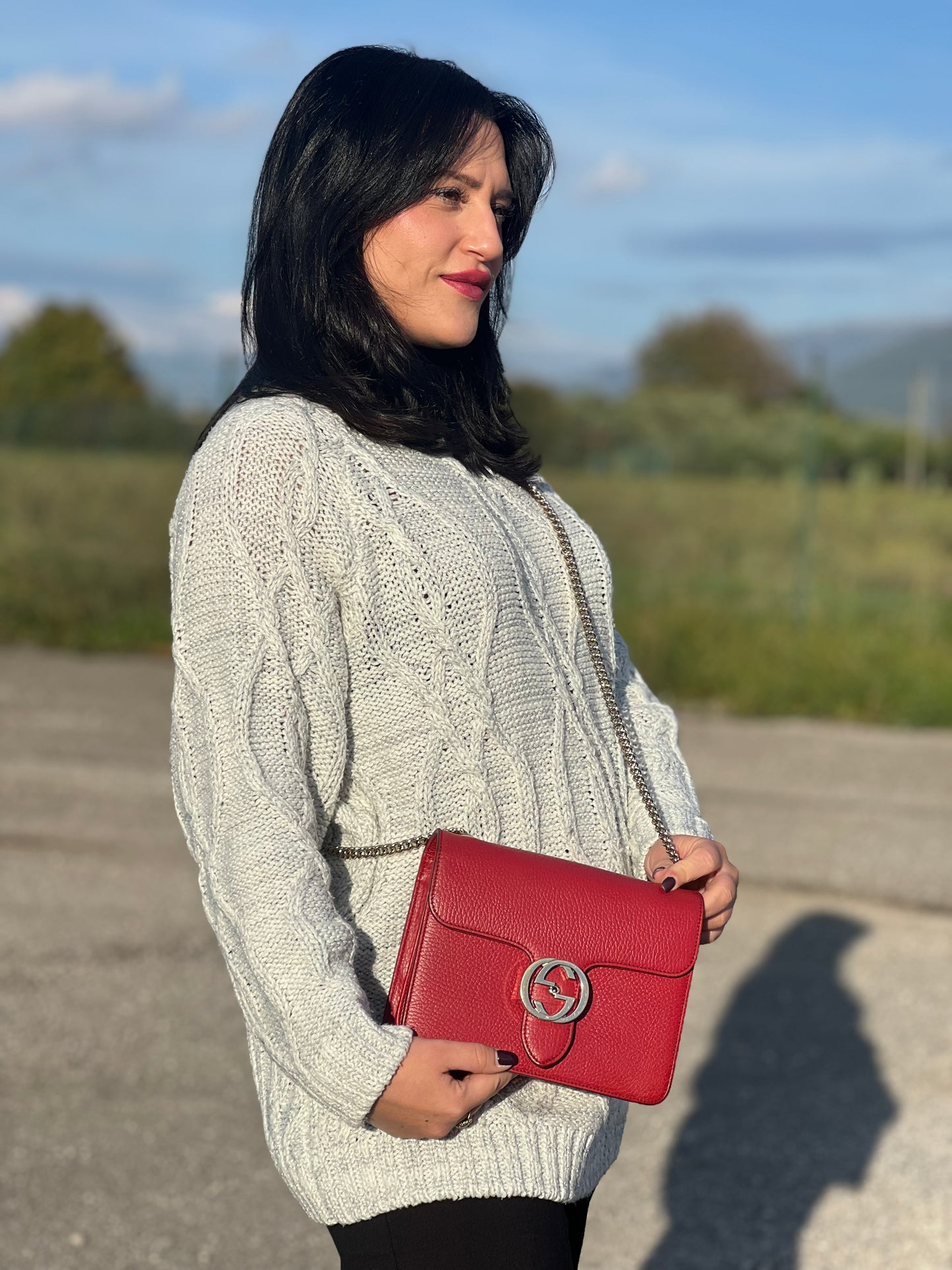 Ragazza che indossa una borsa Gucci Interlocking in pelle martellata rossa con parti metalliche dorate. Munita di una tracolla scorrevole in catena non amovibile e spallaccio in pelle. Chiusura con doppie G incrociate. Completa di dustbag. Indossabile a spalla o a tracolla.