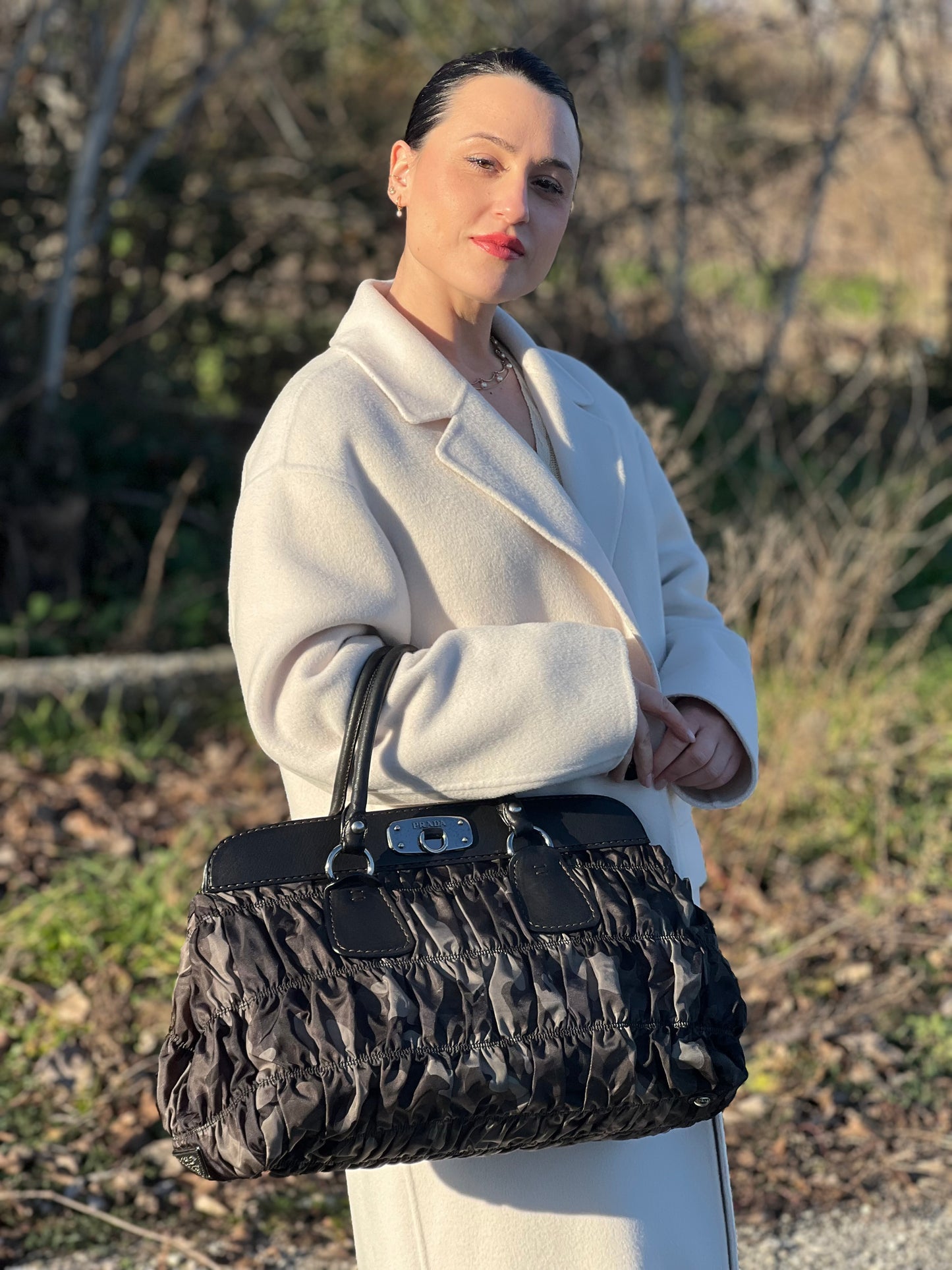 Ragazza che indossa una Borsa Prada in tessuto nylon goffrato trama camouflage nelle tonlità del verde, finiture in pelle nere e inserti metallici argentati; dotata di doppi manici stondati. Completa di dustbag. Originale, usata, di lusso, in ottime condizioni.