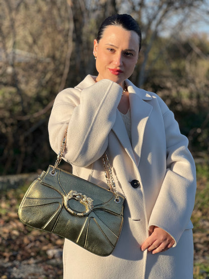 Ragazza che indossa una borsa Gucci in pelle color oro anticato, dettaglio gioiello circolare sulla patta di chiusura composto da due teste di drago contrapposte, smaltate e decorate con micro strass, parti metalliche dorate; munita di doppi manici in catena a maglie. Indossabile a spalla.