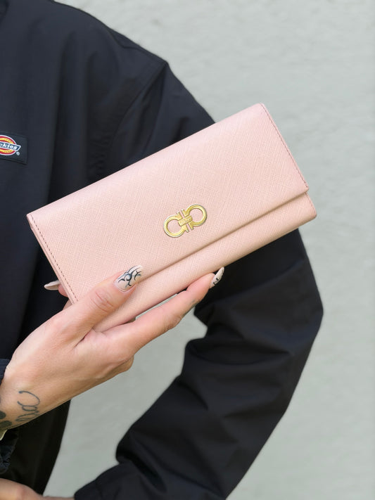 Ragazza che indossa un portafoglio Salvatore Ferragamo in pelle rosa con metalleria oro chiaro, usato, originale, second hand, in ottime condizioni.