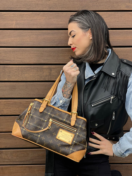 Ragazza che indossa una borsa Louis Vuitton in canvas marrone monogram con cuciture decorative e finiture in vacchetta naturale. Parti metalliche dorate; munita di doppi manici, indossabile a spalla.