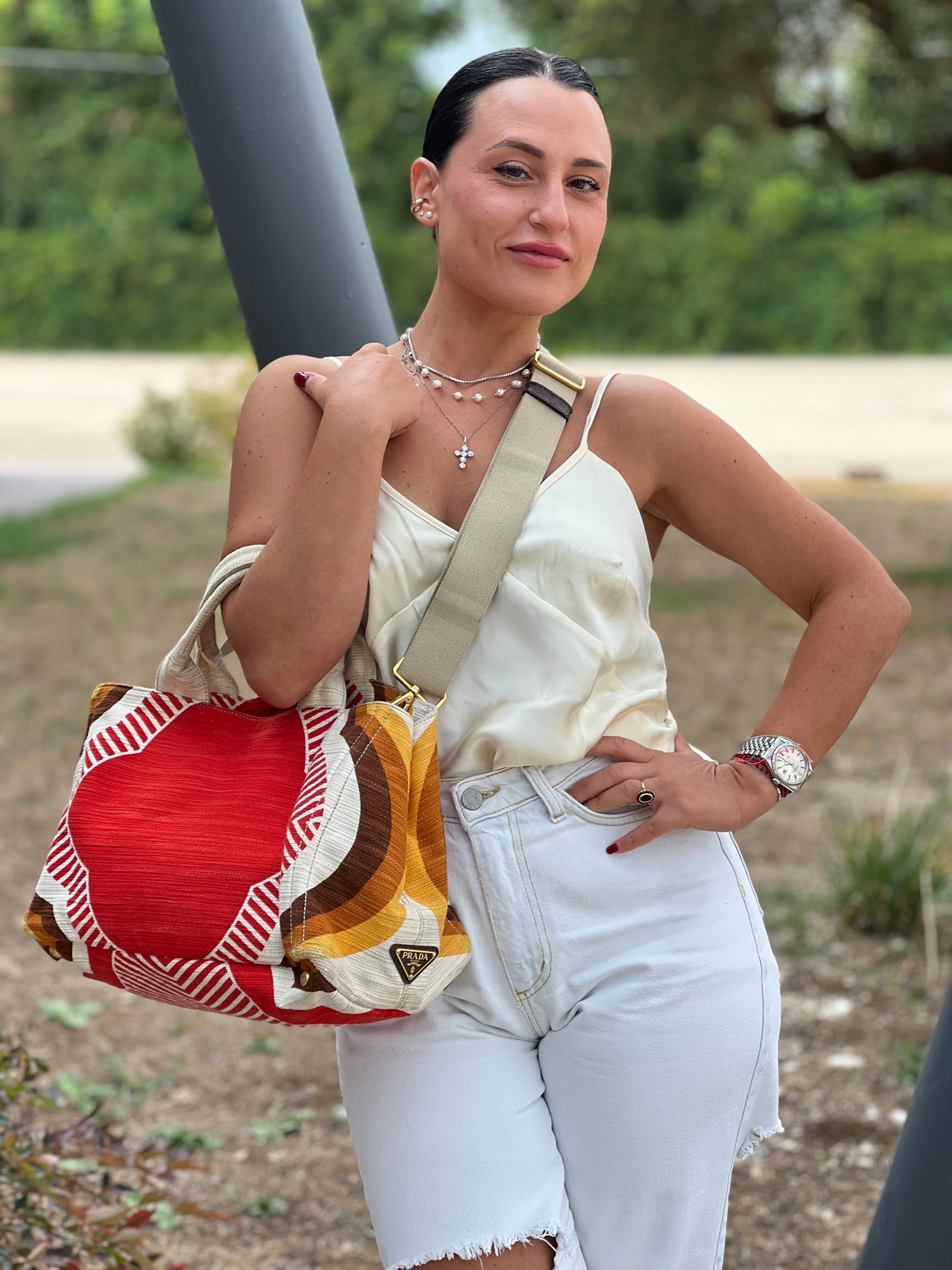 Ragazza che indossa una borsa Prada in tessuto trama multicolore, con inserti metallici dorati; dotata di doppi manici e una tracolla amovibile e regolabile. Indossabile a mano o a tracolla. Completa di card d'autenticità.