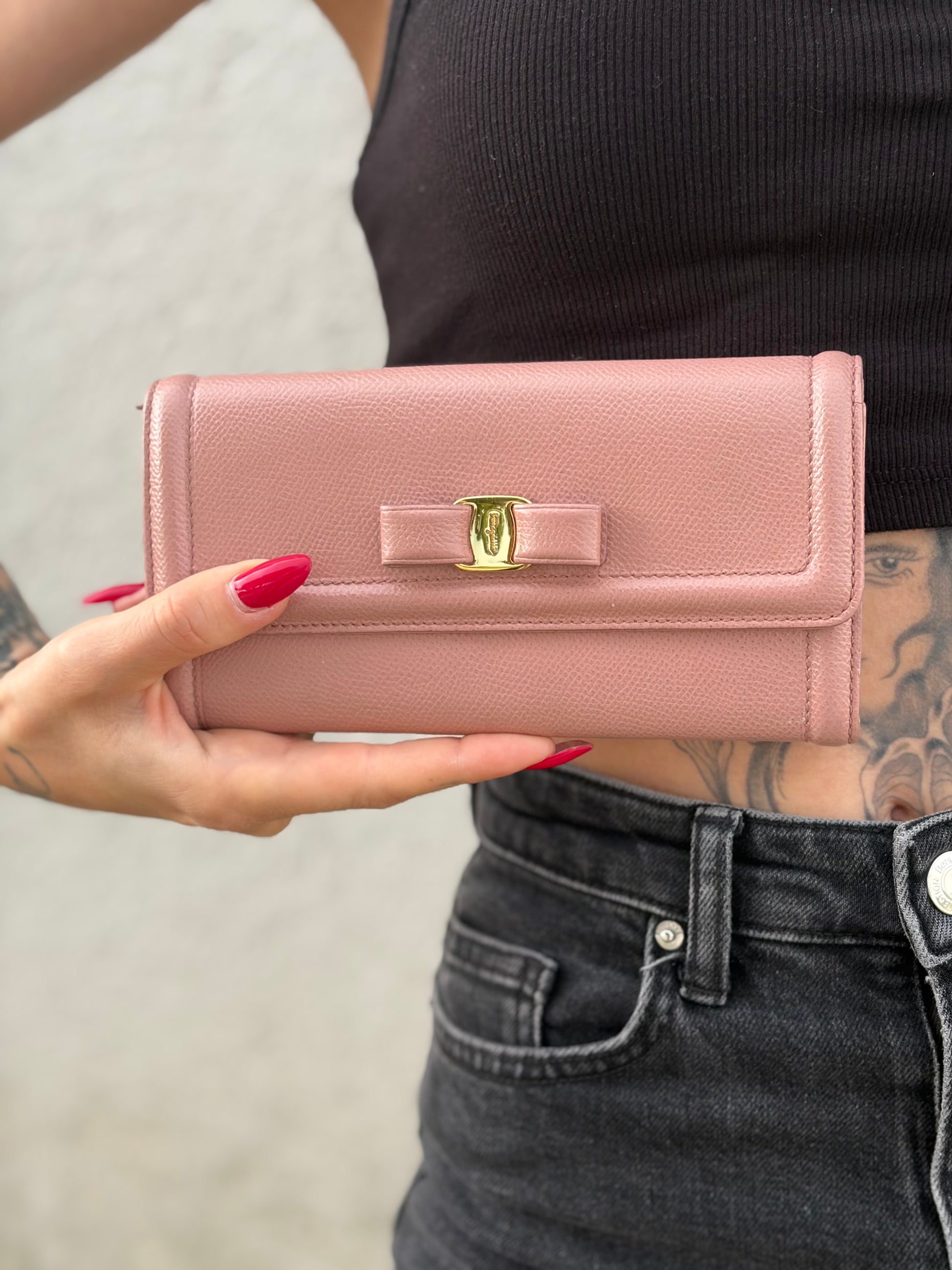 Ragazza che mostra un portafoglio Ferragamo in pelle rosa, dotata di un porta tessera estraibile. Iconico fiocco del brand sul front, usato, originale, second hand, in buone condizioni.