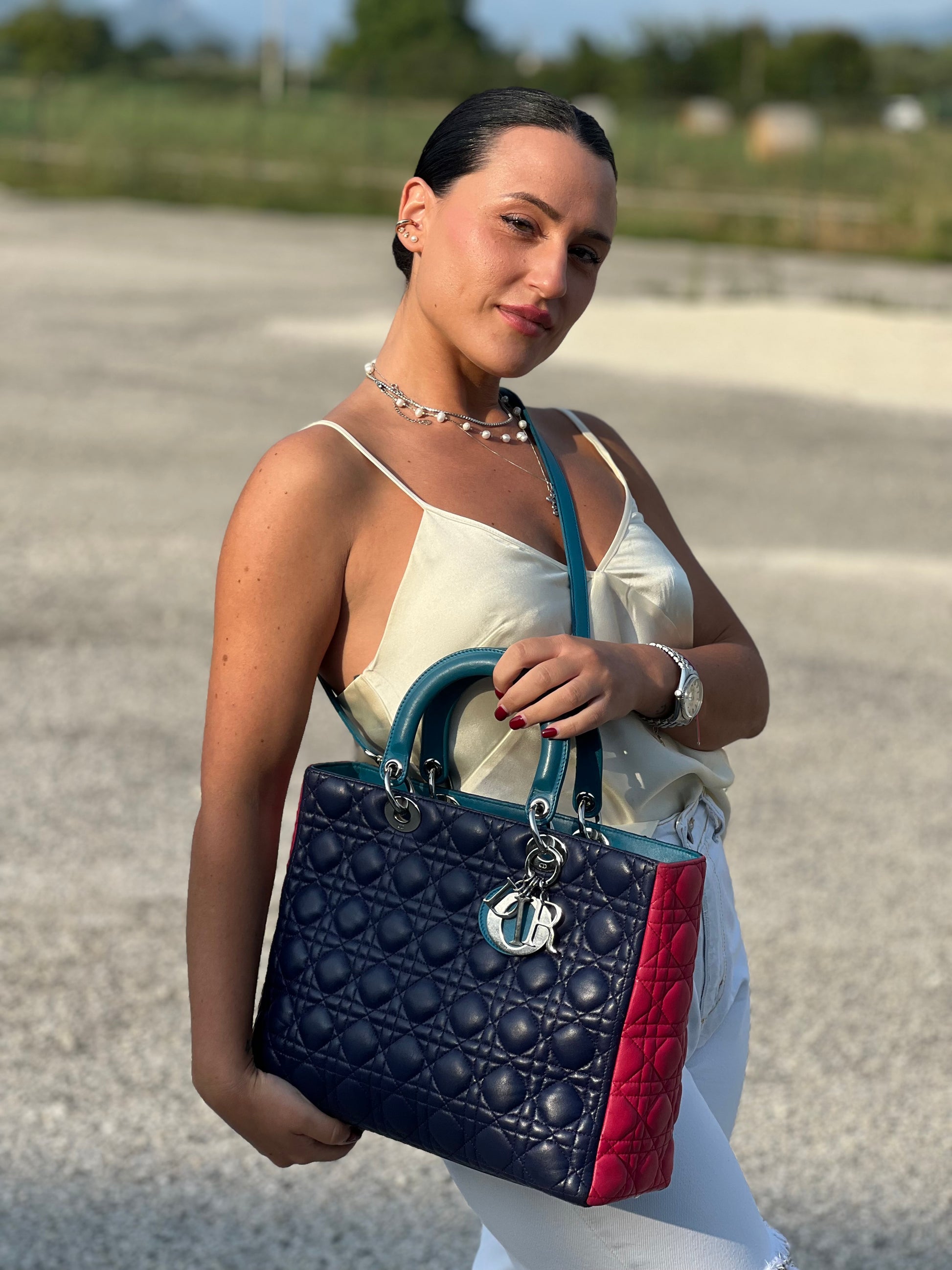 Ragazza che indossa una borsa Lady Dior tricolore in pelle blu, azzurra e fucsia trama cannage. Doppi manici rigidi e una tracolla amovibile, rifinita con parti metalliche argentate. Completa di dustbag.