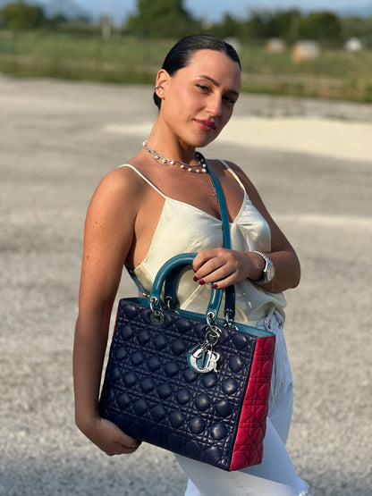 Ragazza che indossa una borsa Lady Dior tricolore in pelle blu, azzurra e fucsia trama cannage. Doppi manici rigidi e una tracolla amovibile, rifinita con parti metalliche argentate. Completa di dustbag.