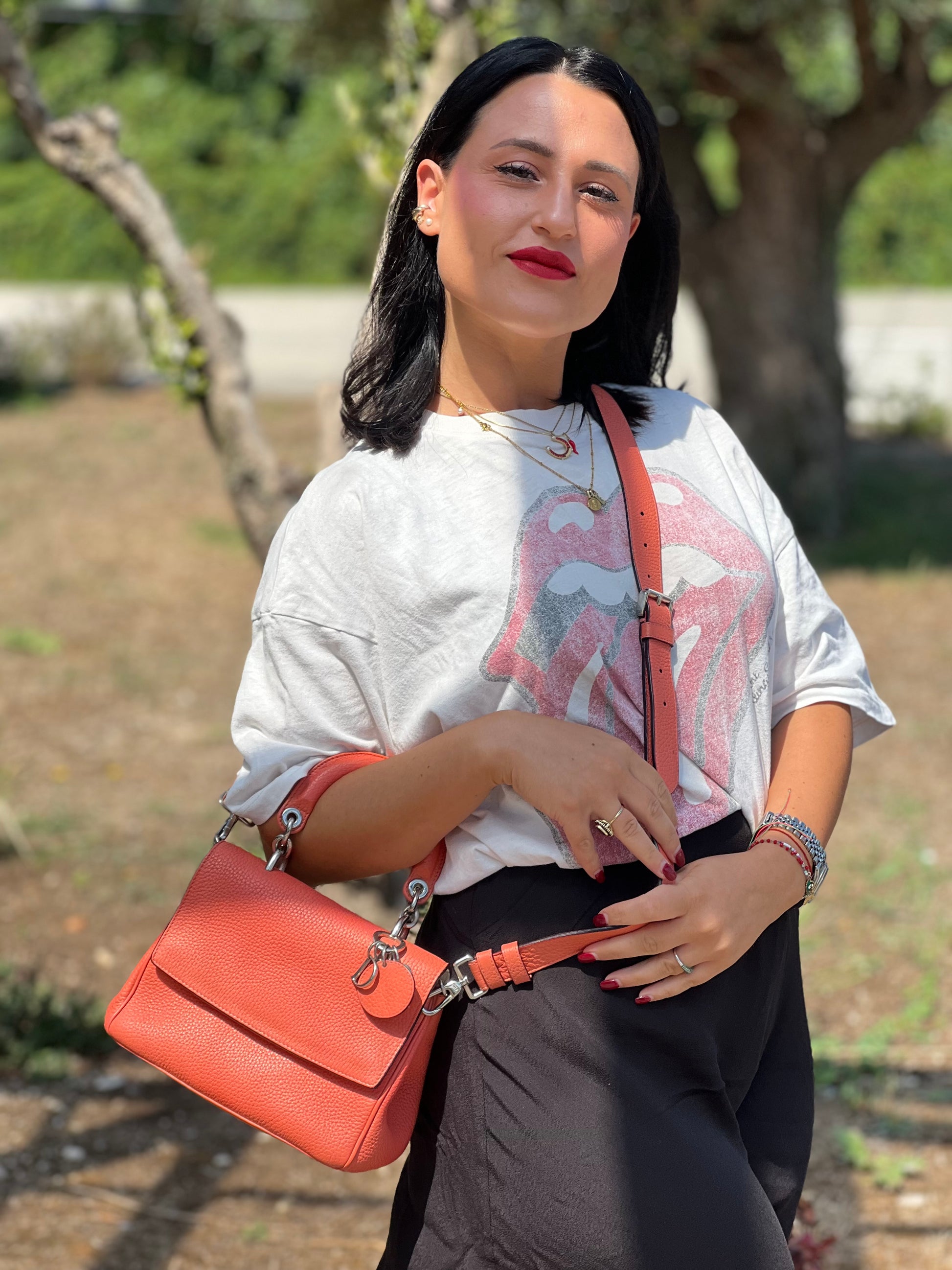 Ragazza che indossa una borsa Christian Dior Bedior in pelle corallo. Manico rigido e tracolla amovibile e regolabile. Parti metalliche argentate.