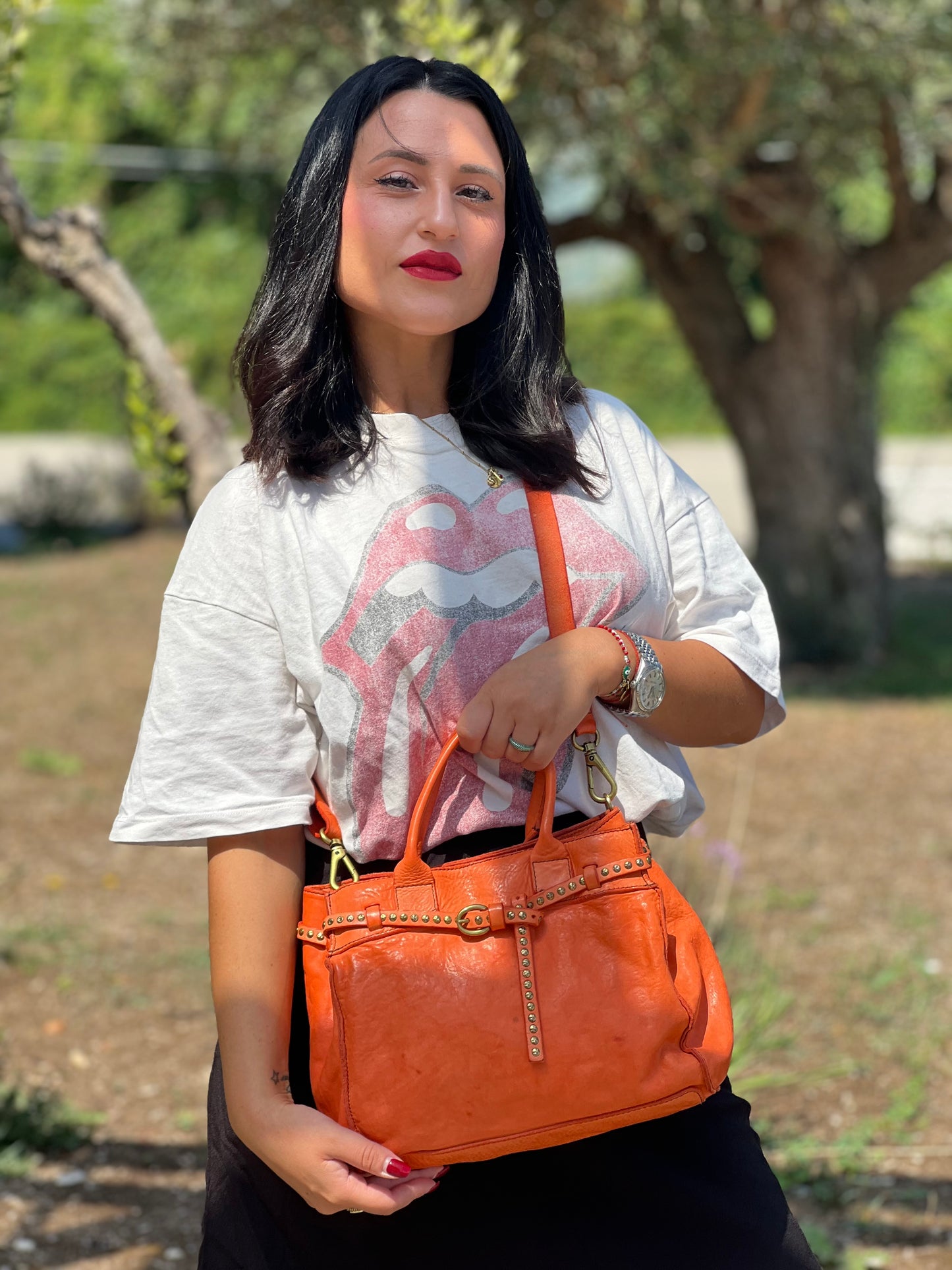 Ragazza che indossa una satchel Campomaggi in pelle arancione; munita di doppi manici e tracolla amovibile e regolabile. Parti metalliche dorate. Completa di dustbag e crema idratante per pelli.
