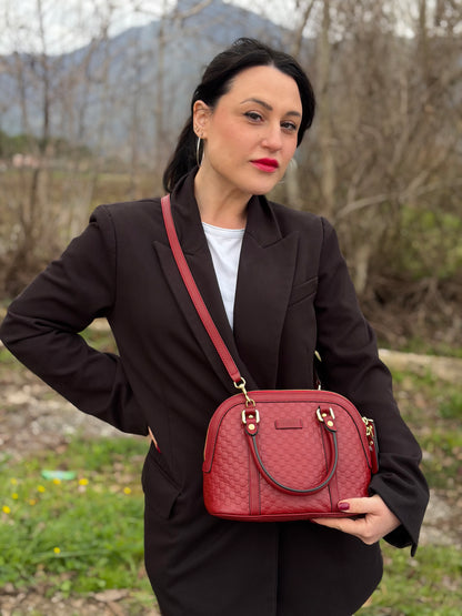 Ragazza che indossa una tracolla Gucci Microguccissima in color rosso ciliegia, con metalleria dorata, usata, originale, second hand, in ottime condizioni.