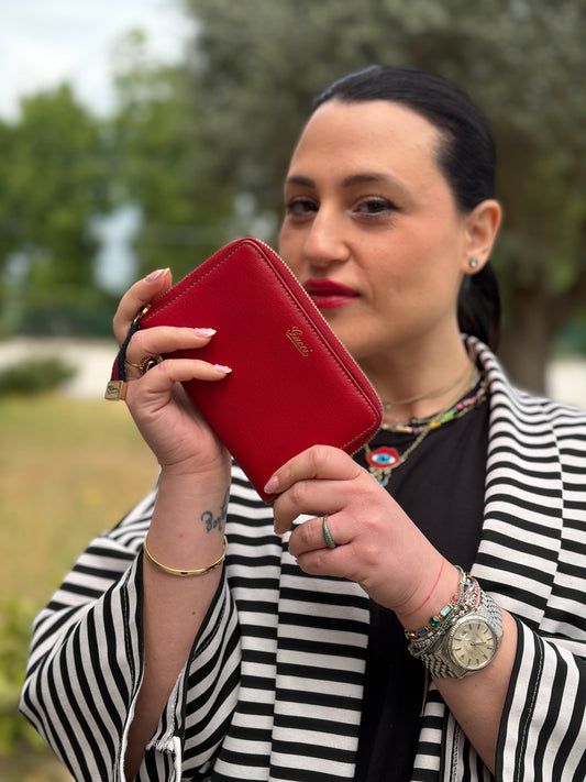 Ragazza che mostra di un portafoglio Gucci in pelle rossa, con tirante in tessuto in iconica trama Web rossa e blu, impreziosito da parti metalliche dorate, usato, originali, second hand, in ottime condizioni.