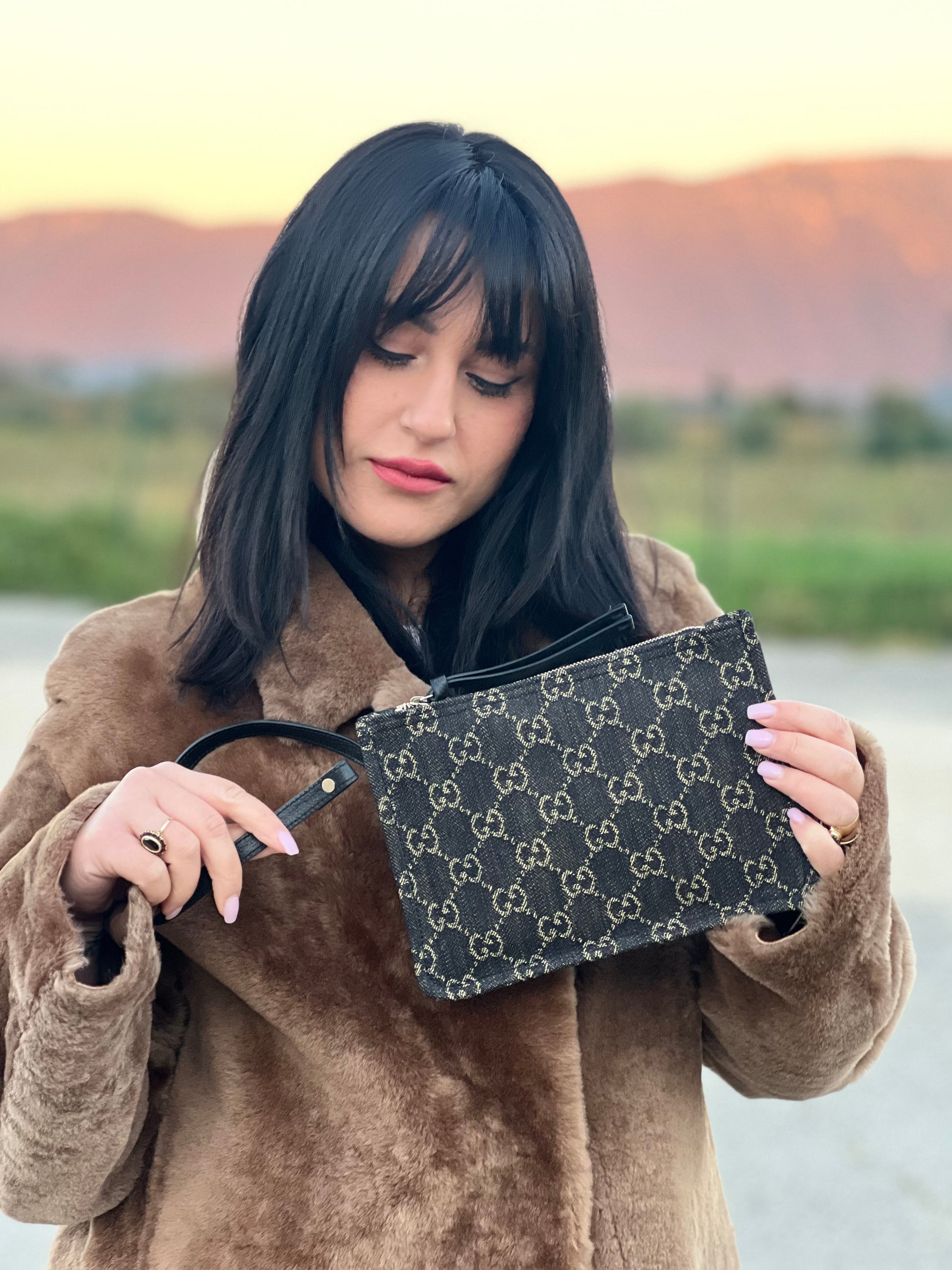 Ragazza che indossa un accessorio pochette Gucci in denim nero trama GG con dettagli in pelle neri. Parti metalliche dorate. Completa di dustbag.