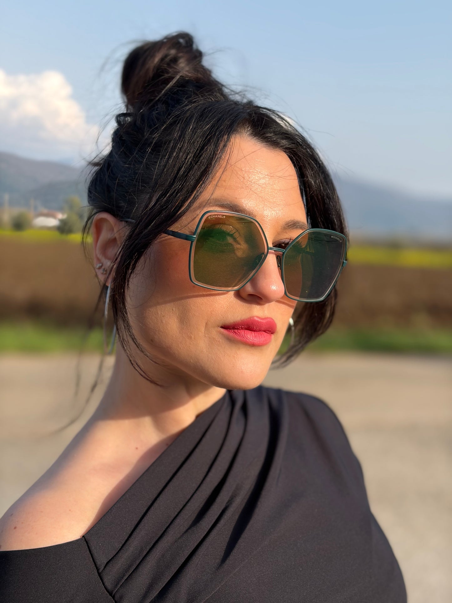 Ragazza che indossa un paio di occhiali da sole Chanel dal design quadrato con aste verde petrolio e lenti cangianti, usati, originali, second hand, in ottime condizioni.