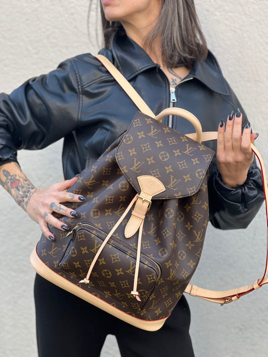 Ragazza che indossa uno zaino LV in canvas marrone monogram con finiture in vacchetta naturale e parti metalliche dorate; munito di due bretelle regolabili. Full set.